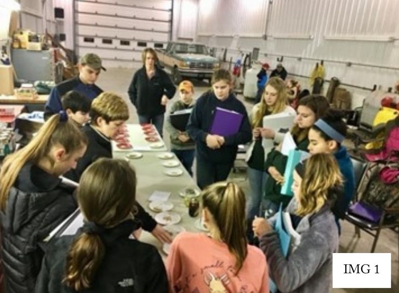 Group of people in a room gathered around food on a plate being instructed on skill-a-thon event