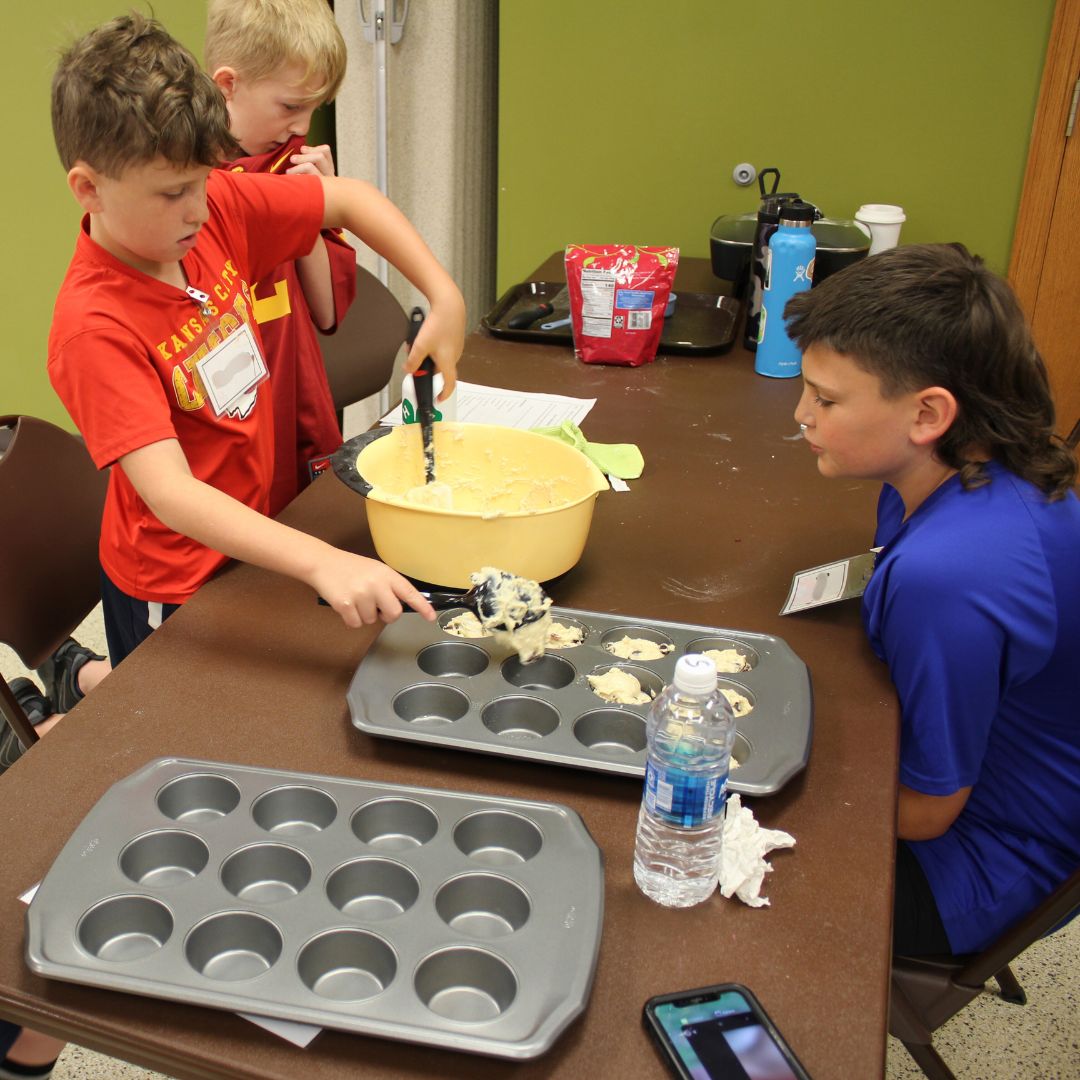 youth pouring cupcake batter into cupcake tin