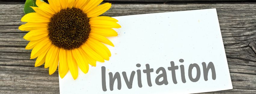 sunflower on the corner of a white paper saying Invitation, both located on top of a wooden table