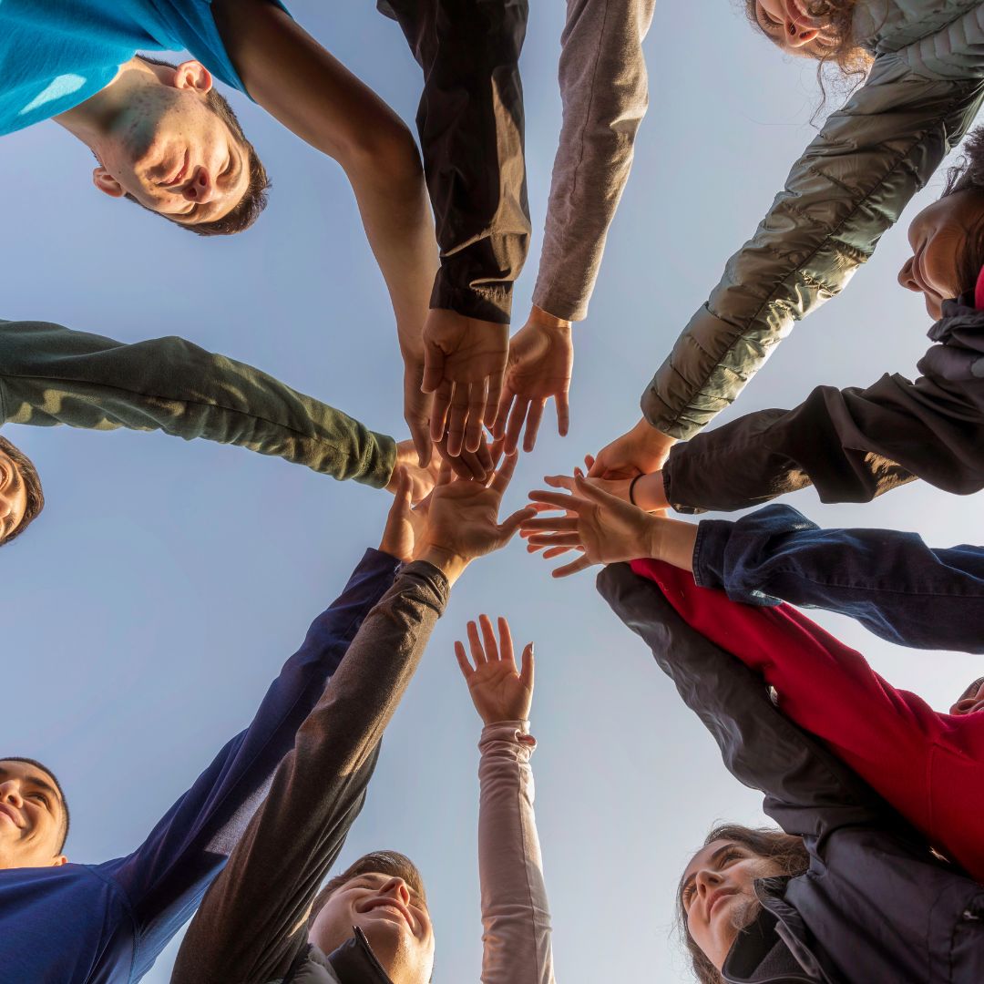 bottom perspective looking up at a circle of various hands joined in the middle