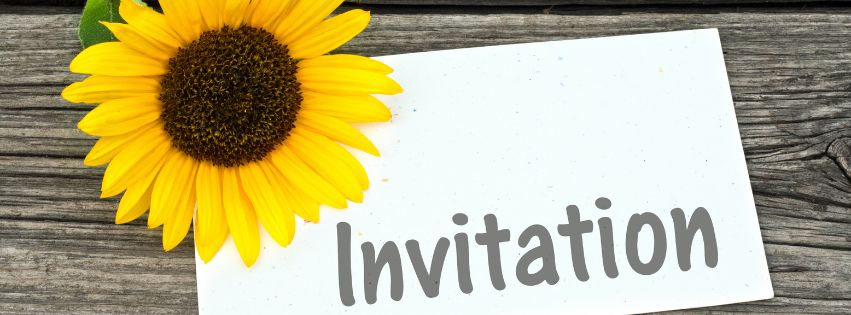 sunflower on the corner of a white paper saying Invitation, both located on top of a wooden table