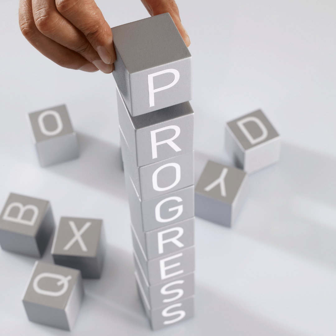 Letter Blocks Stacked on top of one another by a hand spelling out progress