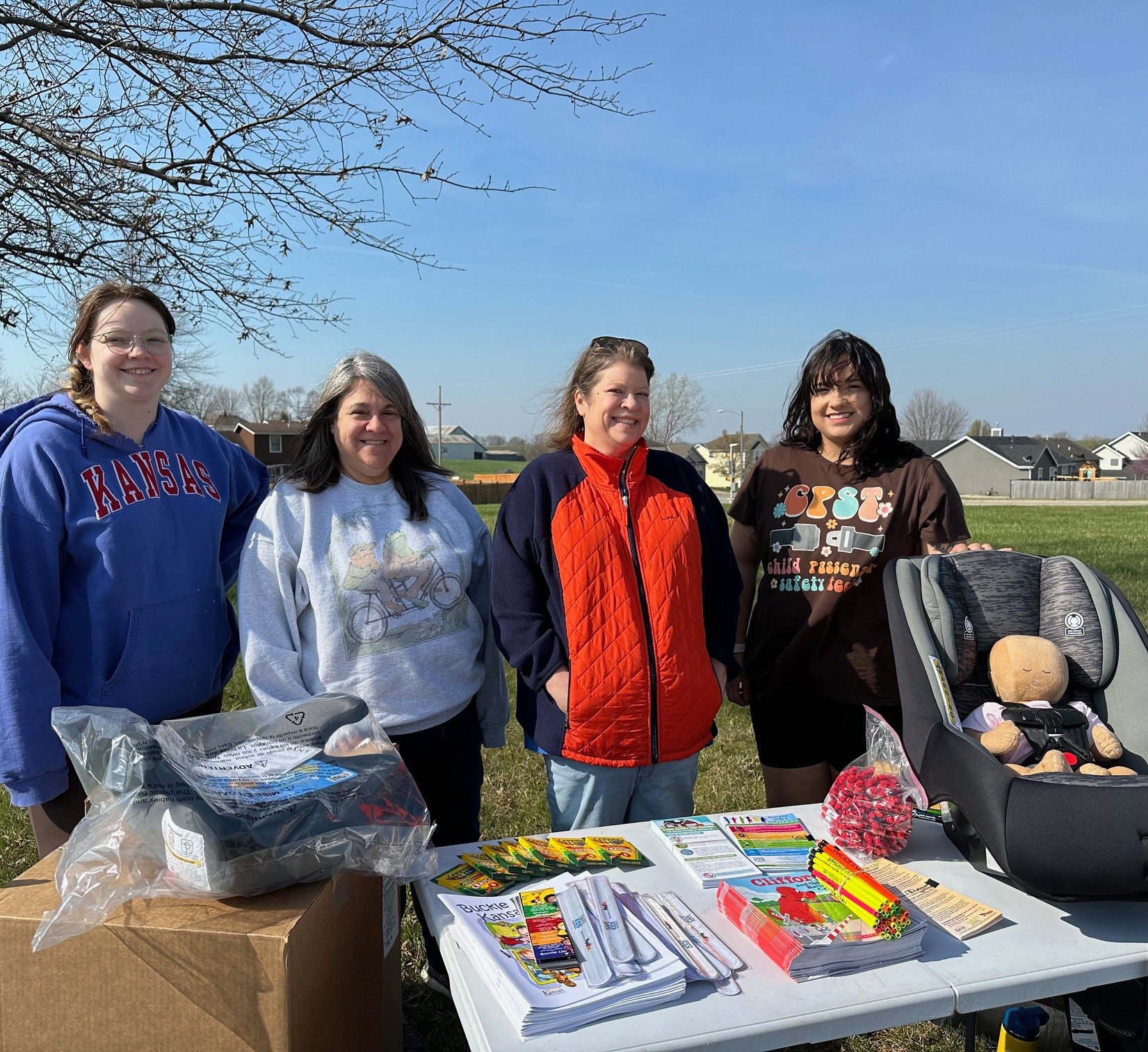 4 females infront of a demonstration table with booster seat and child safety items
