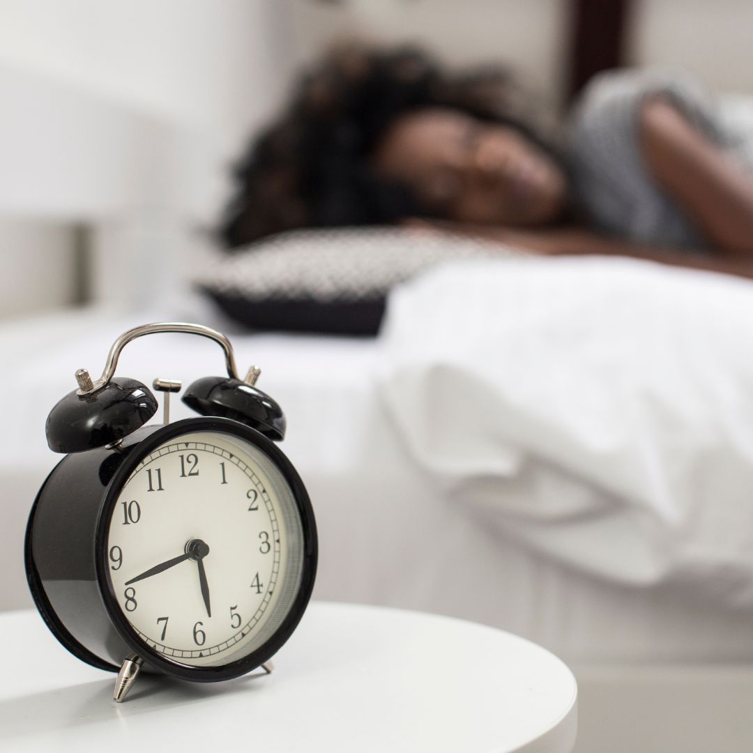 alarm clock in foreground, blurred female in the background blurred sleeping