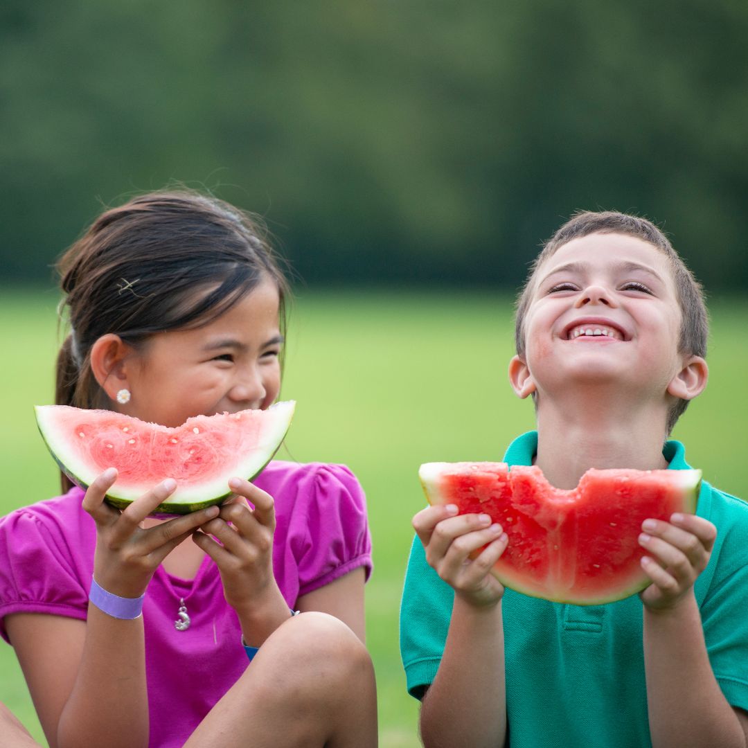 Two kids eating watermelons and smiling. 