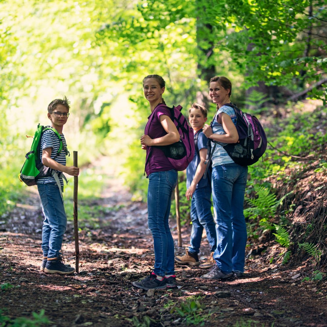 four youth hinking during the day in a dense wooded area are smiling towards the camera